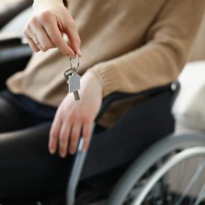 Woman in wheelchair holds keys to apartment. Getting social housing. Home buying concept